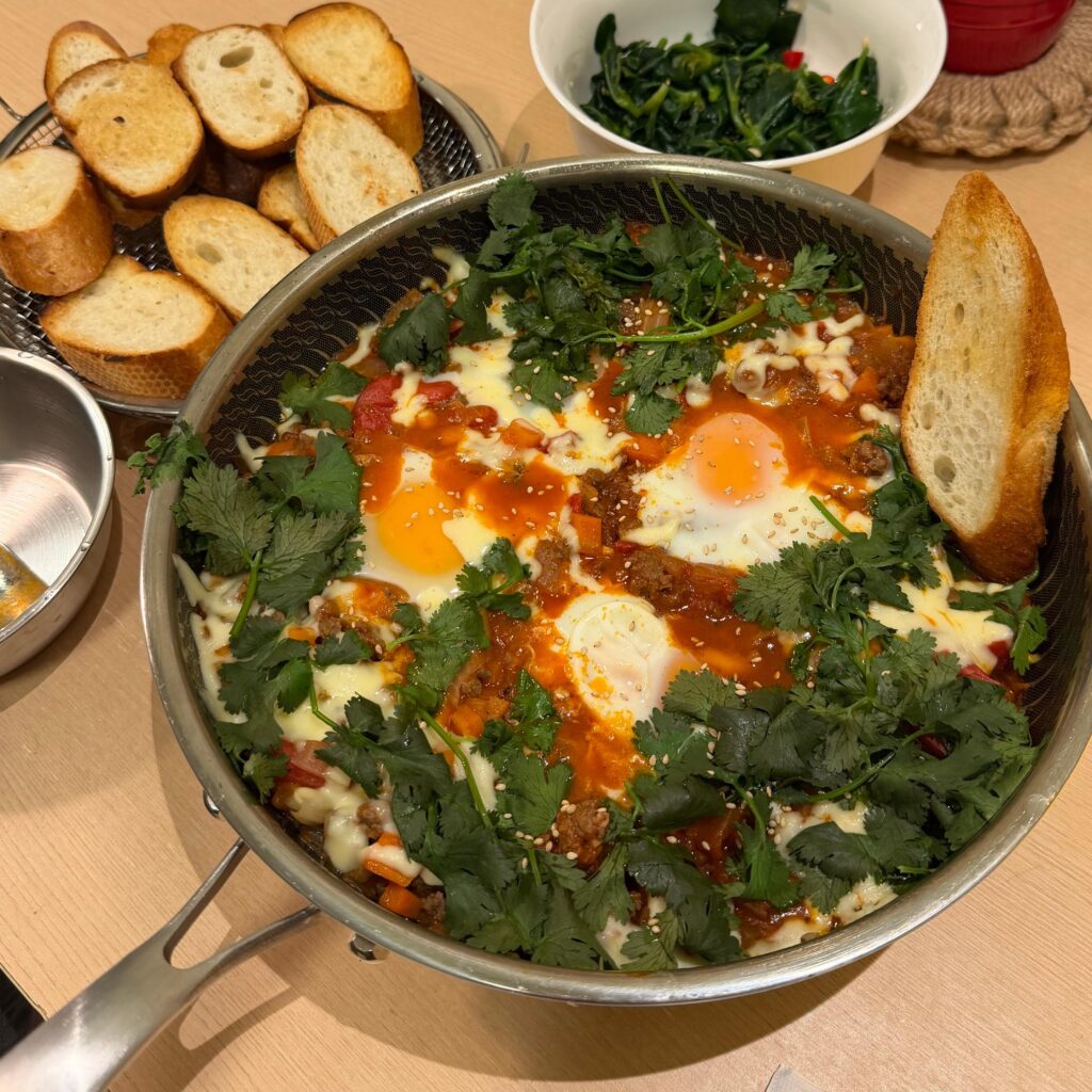 A rustic pan of Shakshuka with poached eggs and tomato sauce, served with fresh French baguette slices on the side.